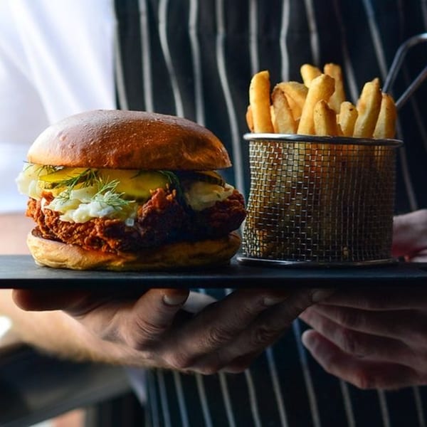 A Drip burger with pickles and sauce, served with a side of fries in a metal basket.