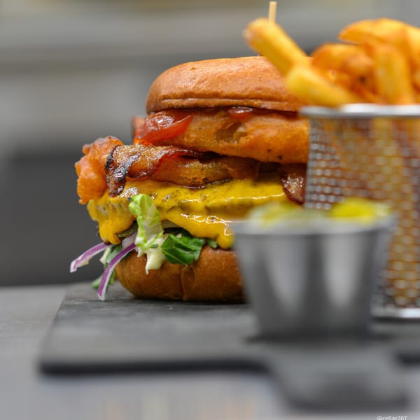 A Drip burger with melted cheese, lettuce, red onion, and onion rings, served with fries.