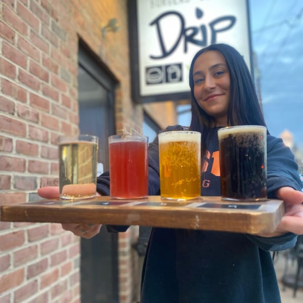 A woman holds a flight of four different Drip craft beers and ciders outside the restaurant.